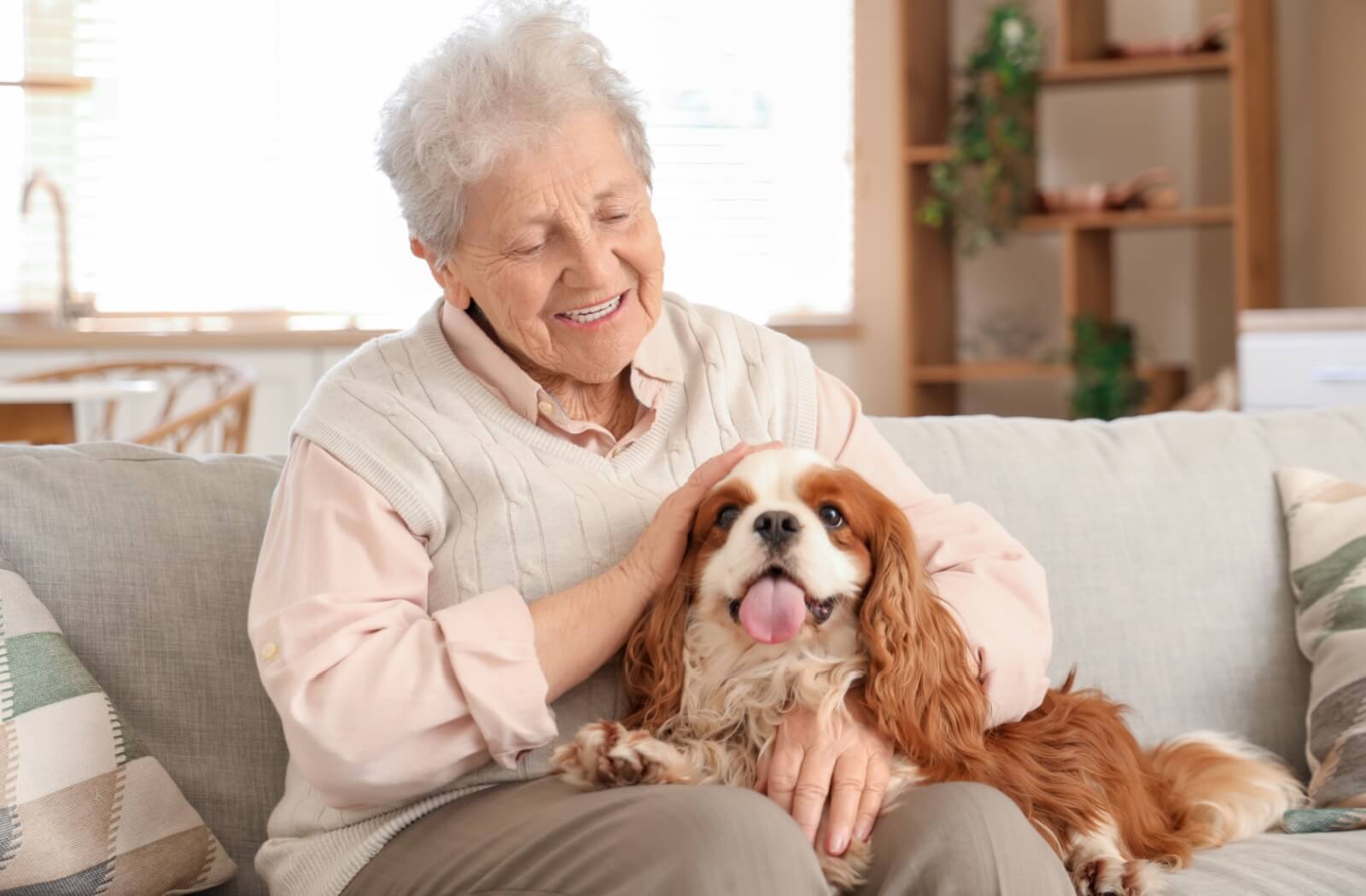 A senior resident sits on a couch with their dog on their lap.