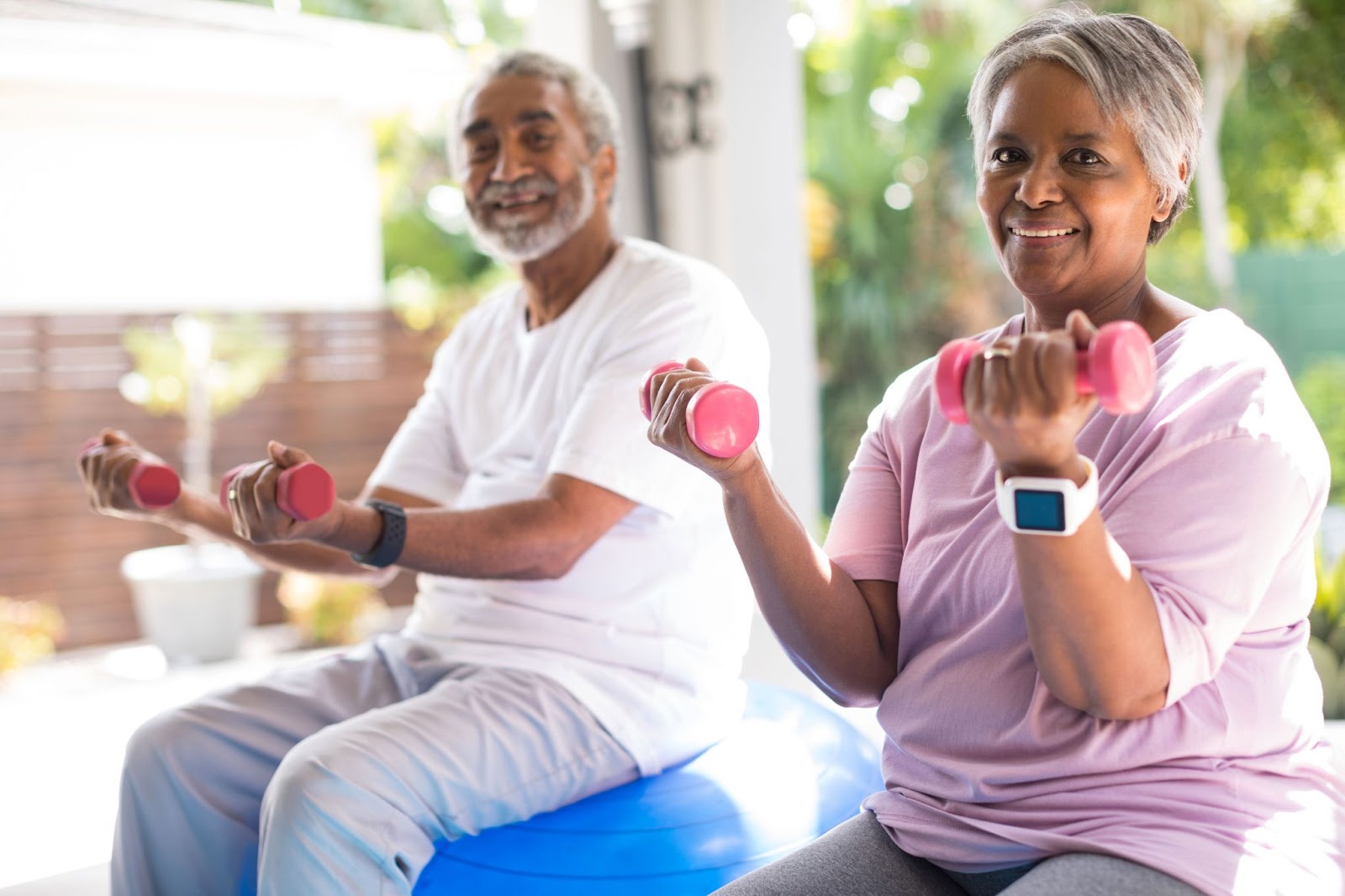A senior couple works out with pink dumbbells while sitting on exercise balls.