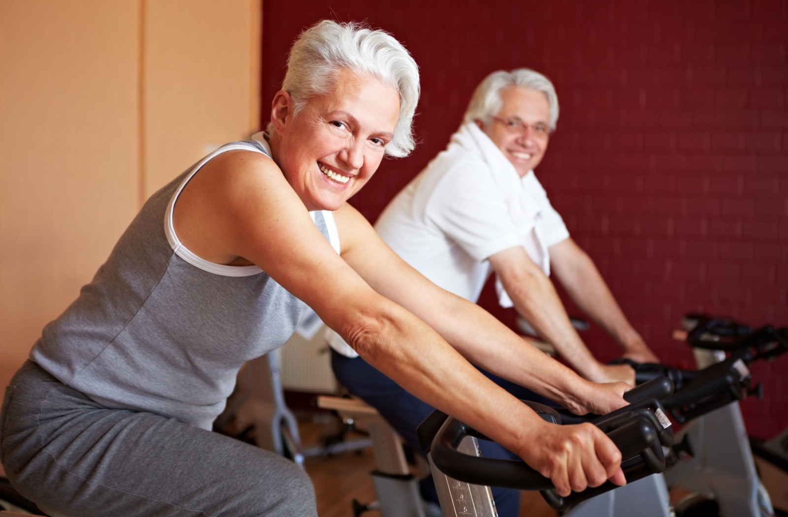 A smiling pair of older adults using exercise bikes to improve their cardiovascular health.