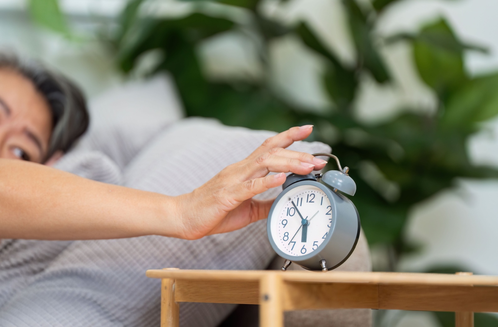 A senior with dementia turns off an alarm on the bedside table set for 5:50 AM, adhering to a regular early morning routine