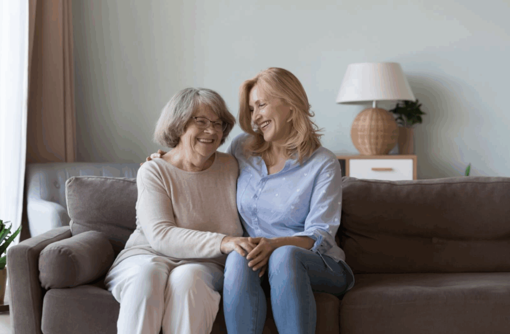 An adult and their older parent share a hug on the couch, using physical touch to create a warm space for talking