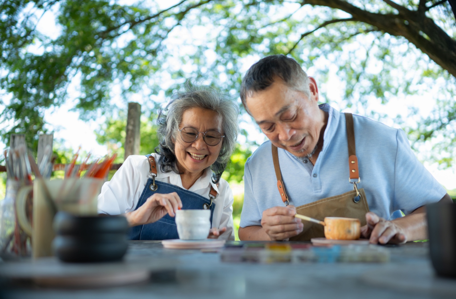 A senior couple paints pottery outdoors.