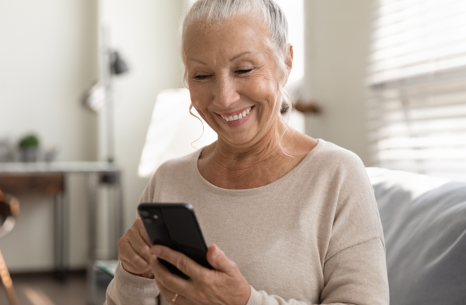 A senior smiles as they browse social media on their smartphone.