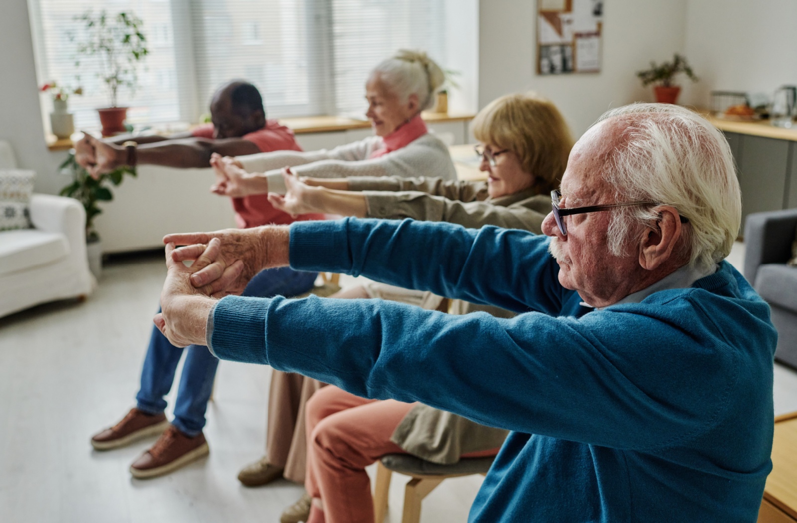 A group of seniors stretch their arms during a fitness class, working on improving their flexibility.