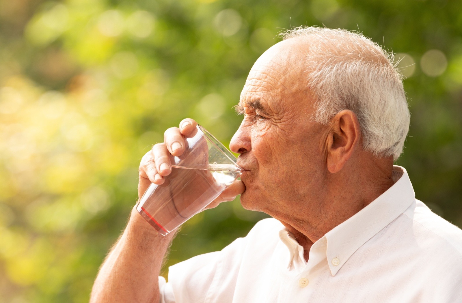 A senior drinks a glass of water while enjoying the warm sun outside.

