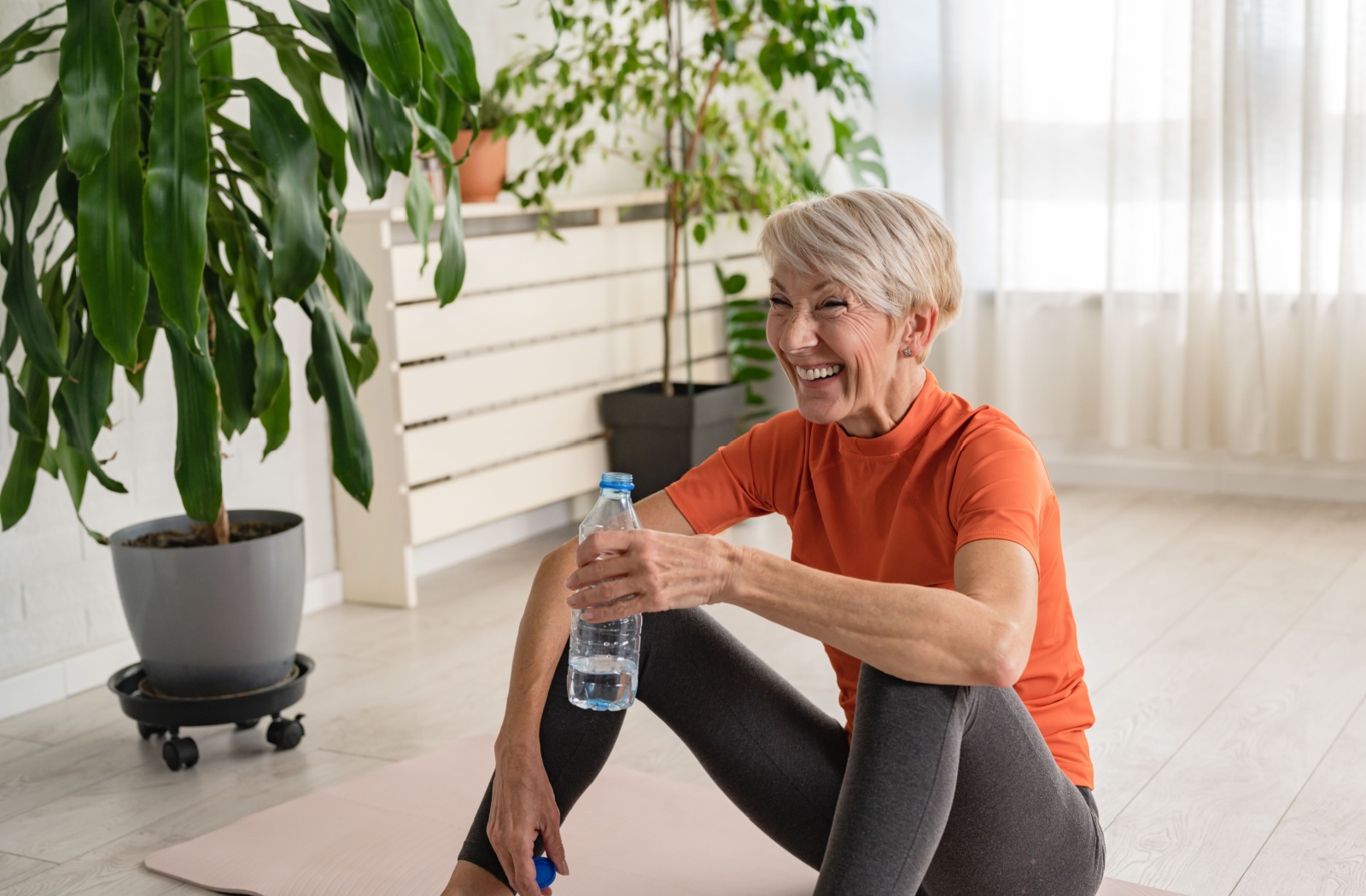 A senior smiles while drinking a bottle of water after participating in a fitness class.