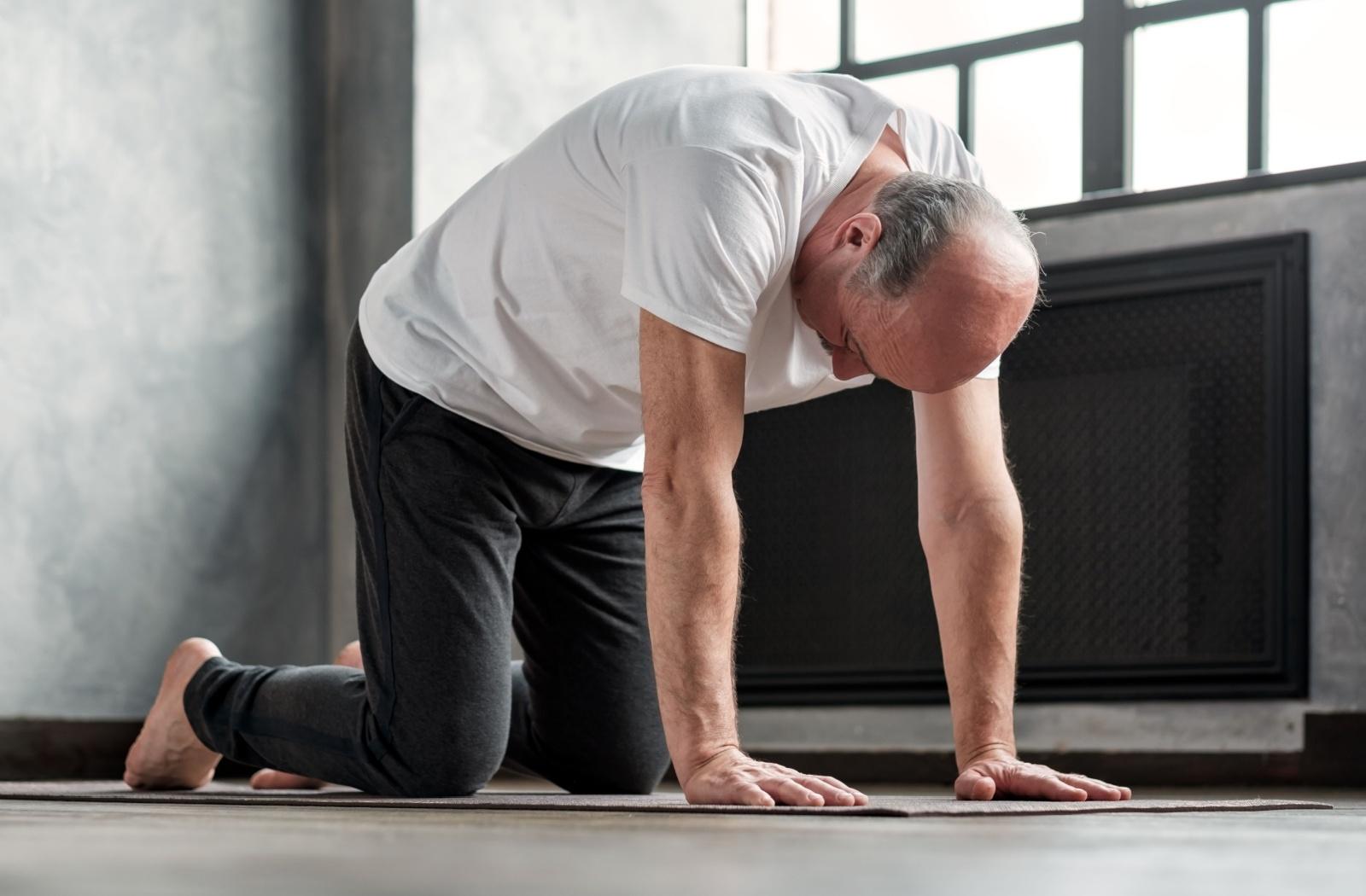 A senior performing the cat cow yoga pose on a yoga mat.