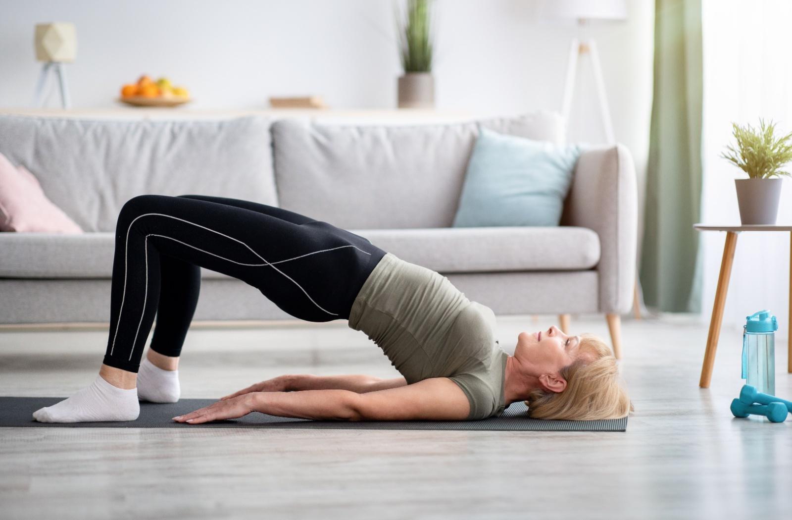 A senior performs hip raises while on a yoga mat in their living room.